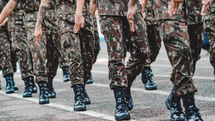 A group of UK Armed Forces personnel in camouflage uniforms and black boots march in formation on a paved surface.