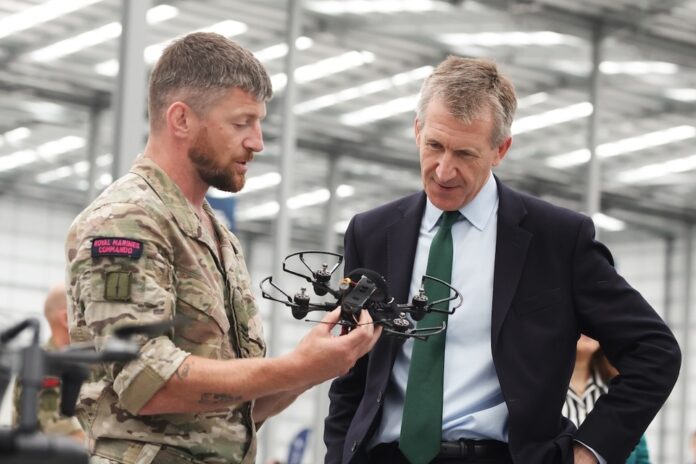 A man in military uniform shows a small drone to a man in a suit inside an industrial building at a drone testing centre in Swindon, Europe.